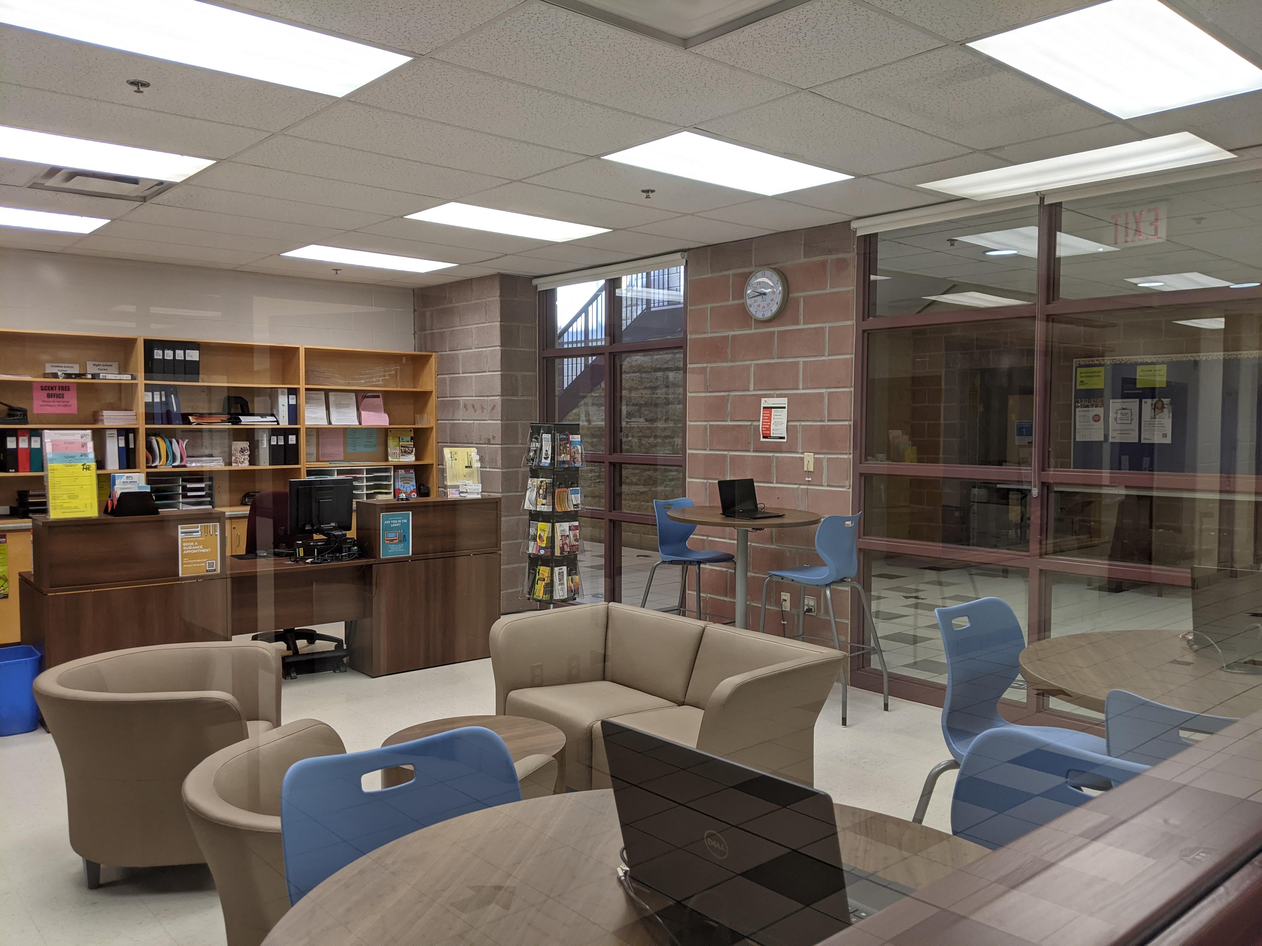 view of large office with brick wall and glass windows. Comfortable-looking couches and chairs in the middle of the room.
